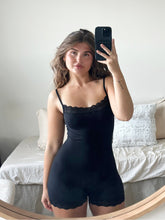 Woman in a black Florence by Mills romper with lace trim, taking a mirror selfie. Millie Bobby Brown wears red knitted crop top and trousers